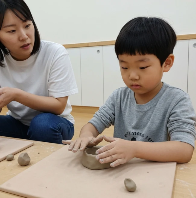 성인 옆에서 두 손으로 점토를 누르고 모양을 만드는 아동