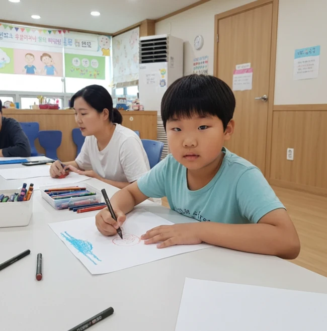 색연필과 종이를 놓고 책상에서 그림을 그리는 아동
